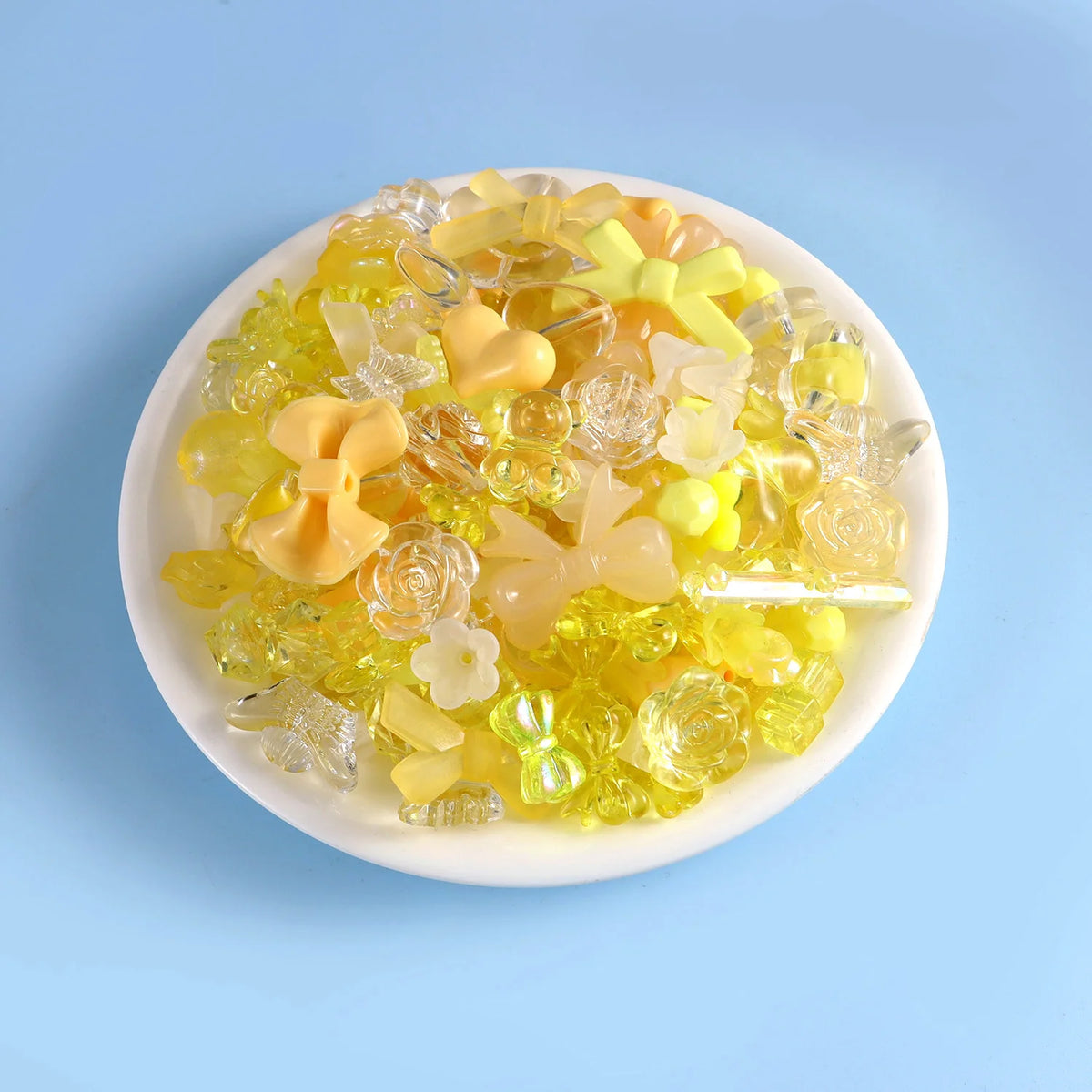 A mix of yellow and clear acrylic beads for DIY jewelry making displayed on a white plate.