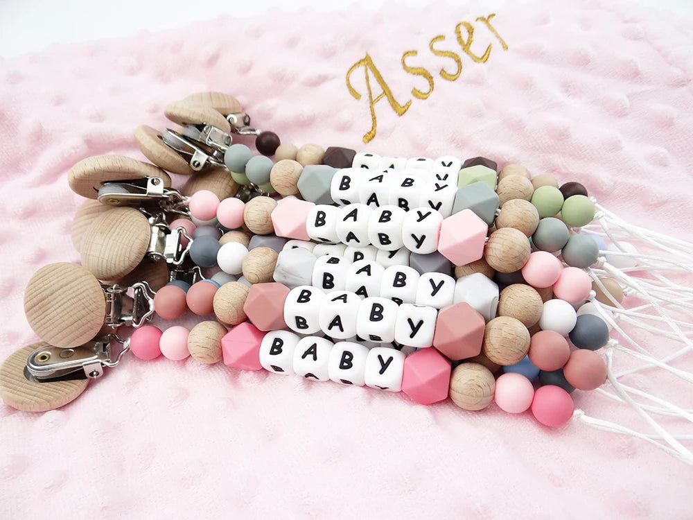 A string of silicone teething beads and clip attachments in various pastel colors and white baby name tiles.