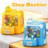 A yellow and blue mini claw machine toy for kids with a gift surprise feature displayed on a wooden surface.
