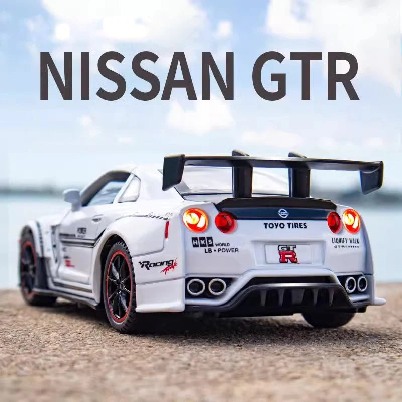 A white Nissan GTR model car with a black spoiler and racing decals is shown outdoors.