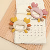 Pink and orange crab-shaped silicone baby teethers resting on a calendar page.