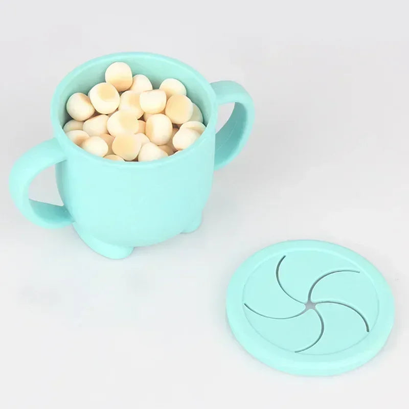 A light blue silicone snack cup filled with small, pale yellow snacks and a matching lid.