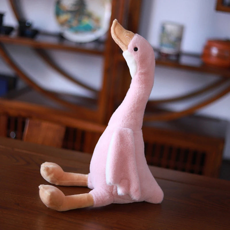 A pink plush toy of a long-necked goose with a curved neck, resting on a wooden surface.