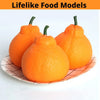 Three realistic orange fruit models resembling small pumpkins or squashes displayed on a paper surface.