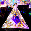 A handcrafted resin dodecahedron die set with light purple and gold numbers resting on a reflective surface.