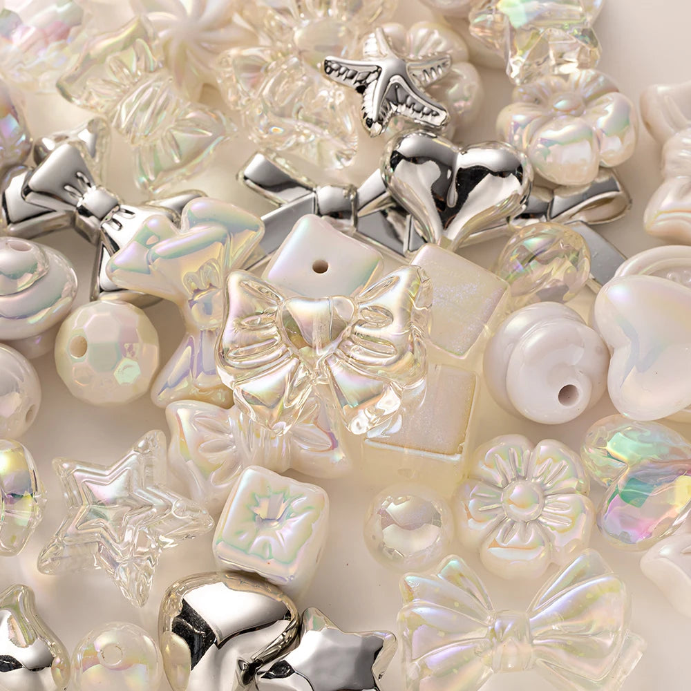A close-up of various iridescent and silver acrylic bow and flower beads for DIY jewelry making.