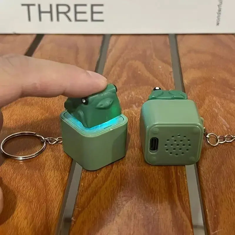A hand holds a green fidget clicker keychain with an LED light and sound feature on a wooden surface.