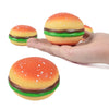 A hand holds a squishy hamburger stress ball with a bright orange top and green bun.