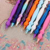 A collection of precision diamond painting pens in various shades of purple, blue, orange, and white arranged diagonally on a