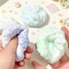 A hand holds a squishy sensory stress ball fidget toy with a marbled light blue and green color.
