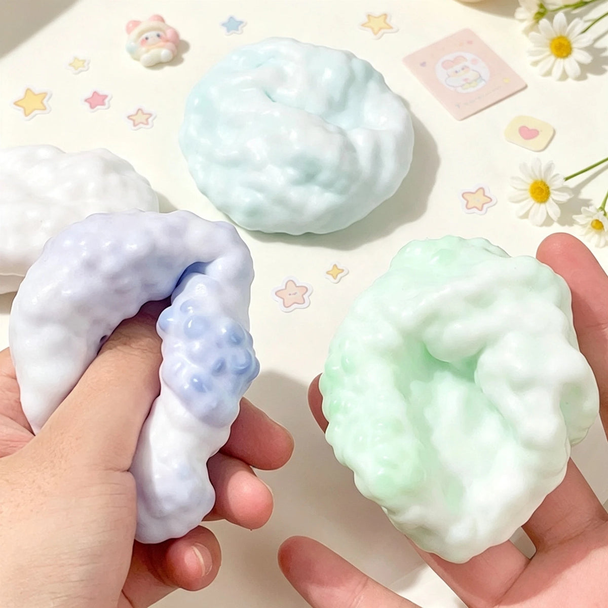 A hand holds a squishy sensory stress ball fidget toy with a marbled light blue and green color.