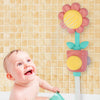 A baby is interacting with a pink and yellow sunflower bath shower sprinkler toy against a light tiled background.