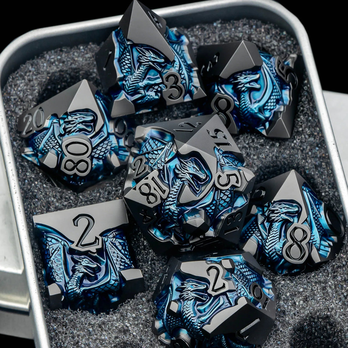 A set of black metal dice featuring a dragon design are displayed in a silver container.