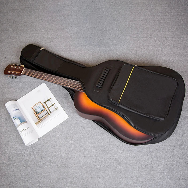 A black acoustic guitar bag is shown next to a guitar and a piece of paper on a gray background.