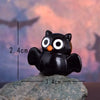 A black cartoon bear figurine with large white eyes and an orange nose is placed on a gray rock.