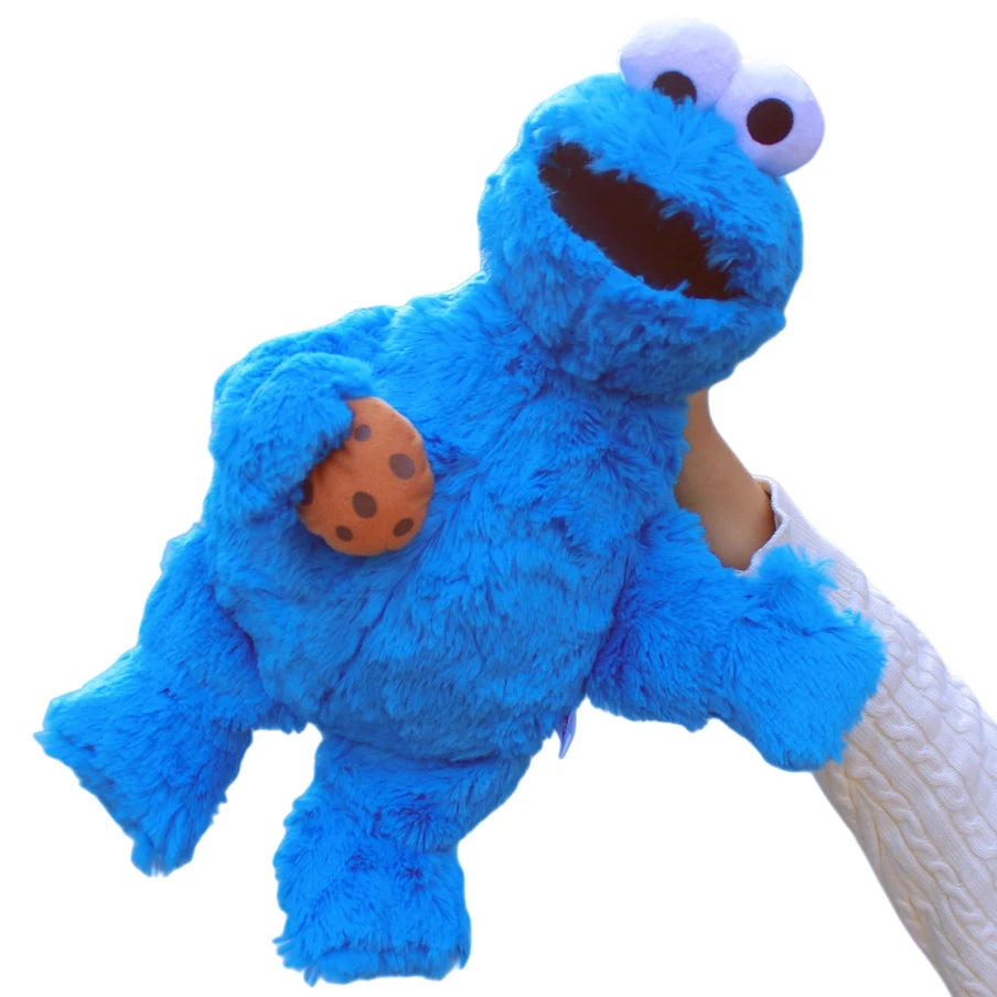 A blue Cookie Monster plush toy with large eyes and an orange cookie detail being held by a person.