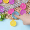 A hand is squeezing a translucent blue squishy fidget toy among various colored squishies in a wire basket on a woven mat.