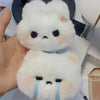 A white plush rabbit charm with black eyes and blue tear lines is held in a hand.