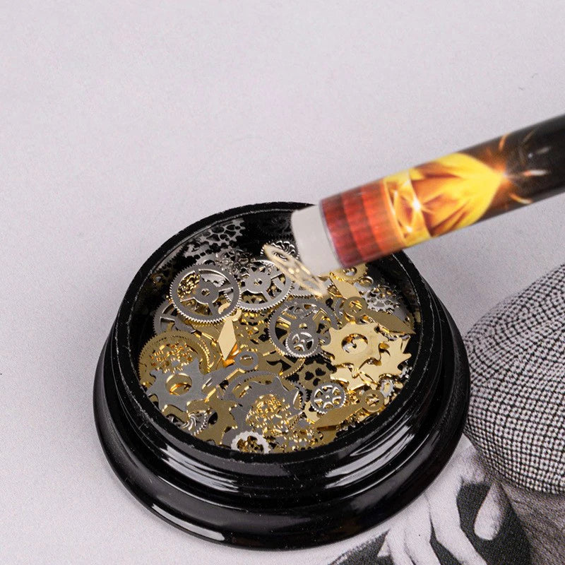 A black glass container holds small gold and silver rhinestones, with a pen tip dripping wax onto the gems.