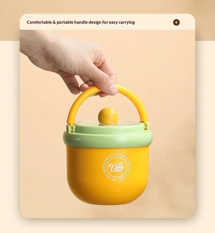 A hand is holding a yellow insulated stainless steel breakfast cup with a green lid.