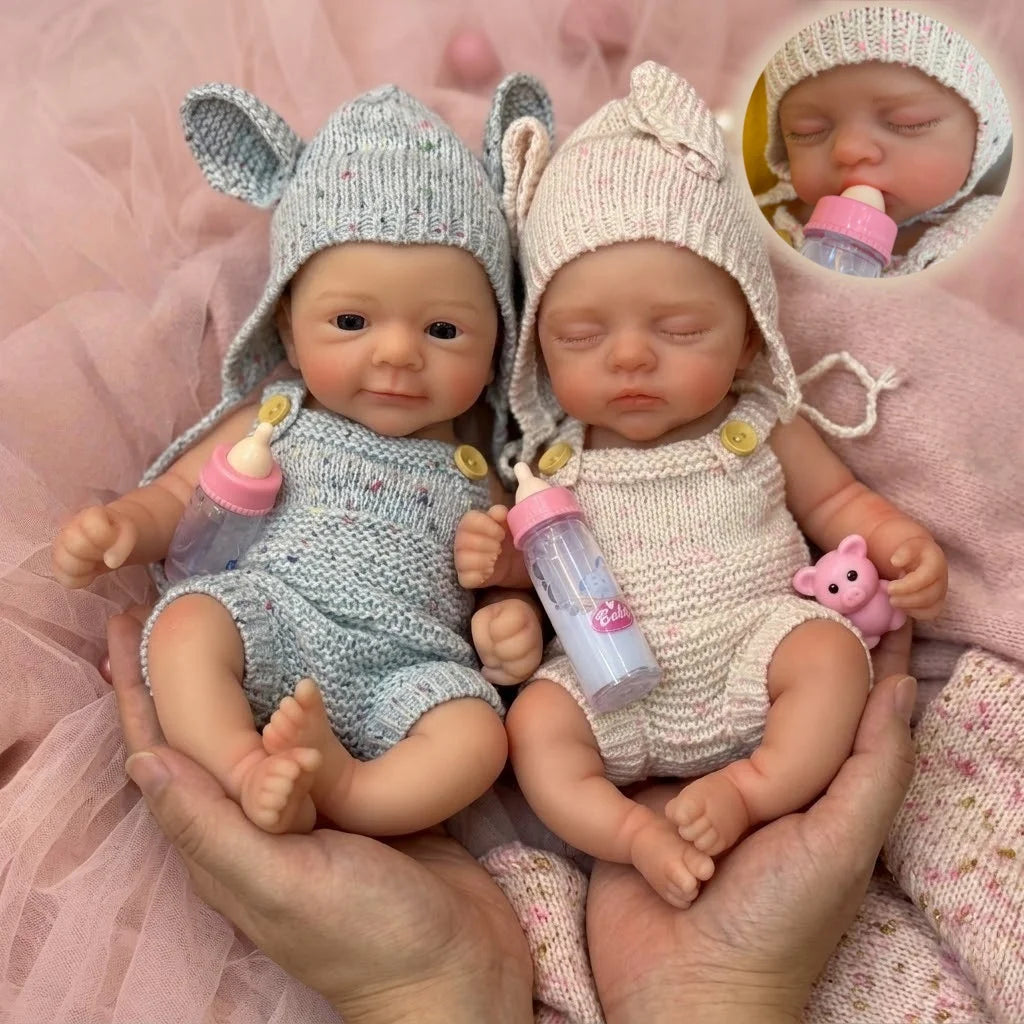 A pair of hand-painted silicone reborn dolls wearing knitted animal hats and holding bottles