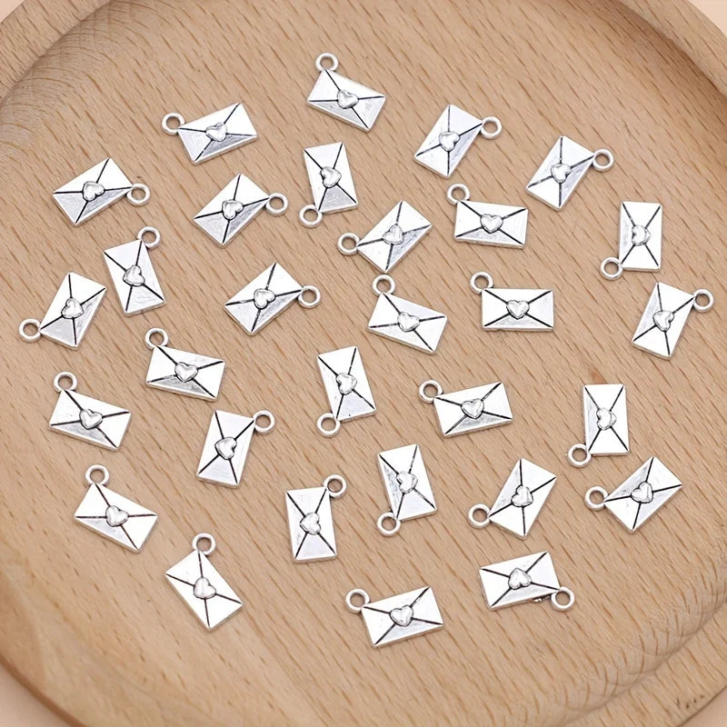 A collection of silver vintage envelope charms for jewelry making arranged on a wooden surface.