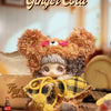 A fluffy brown bear plush charm designed to look like a cookie, featuring pink accents and a yellow plaid accessory.