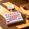A pink keyboard keycap clicker with various colorful and themed keycaps resting on a wooden surface.