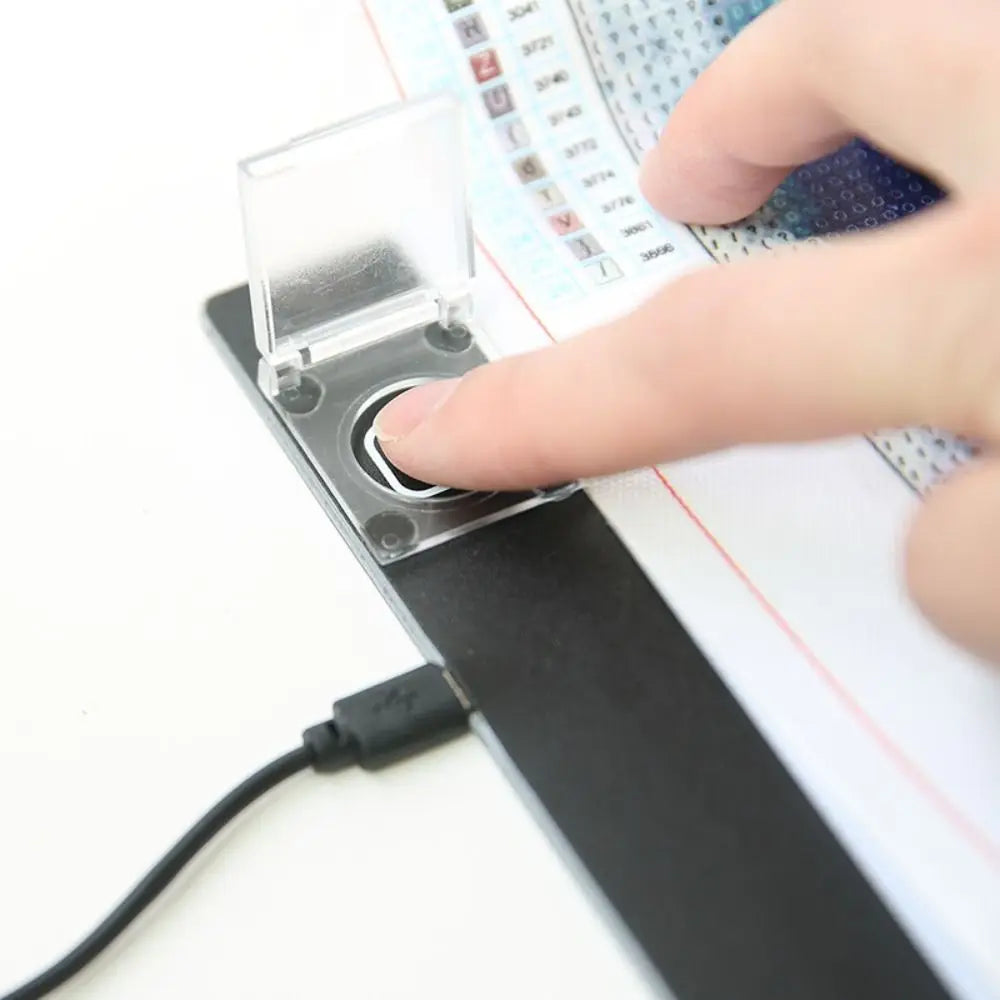 A hand is pressing a clear plastic switch protector cover onto a black light pad device.