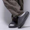 A close-up of a person's leg wearing dark pants and comfortable gray EVA platform slides on their foot.