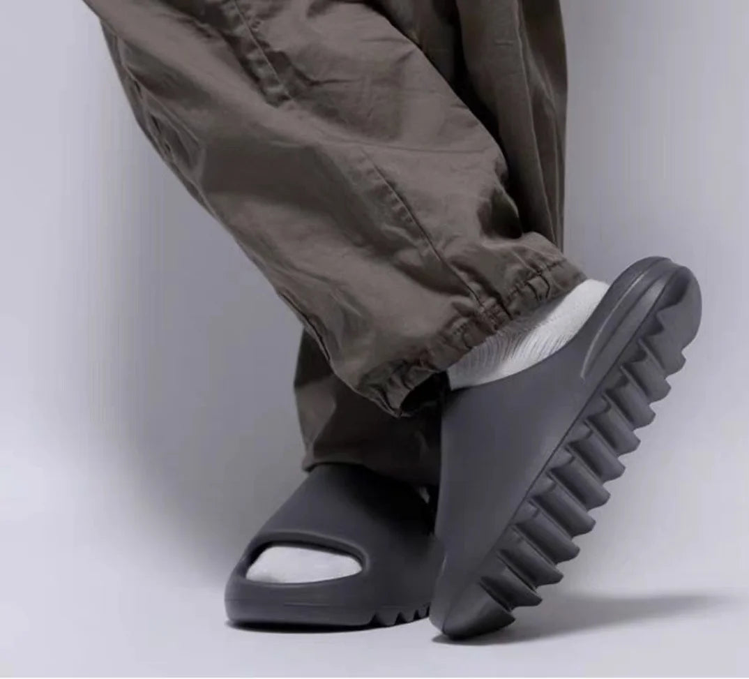 A close-up of a person's leg wearing dark pants and comfortable gray EVA platform slides on their foot.