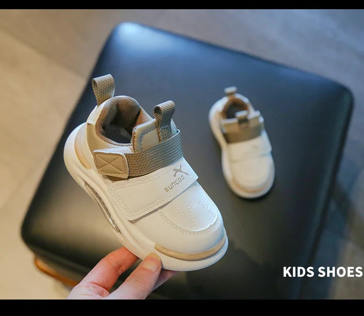 A white kids shoe with gray accents is shown resting on a dark surface.