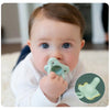 A baby is shown holding a light green silicone pacifier soother.
