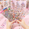 A hand holds a transparent plastic sheet filled with a 12-pack of colorful 3D landscape stickers.