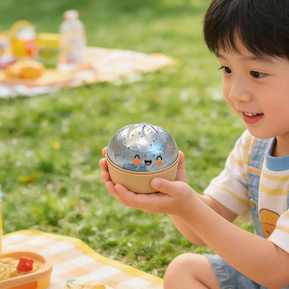 A young boy holds a glitter slow-rising dumpling stress ball with a steamer base outdoors on the grass.