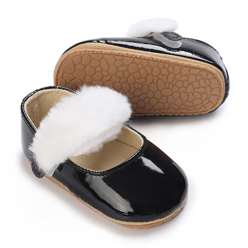 Black patent moccasin shoes for a baby girl with white faux fur trim and bow