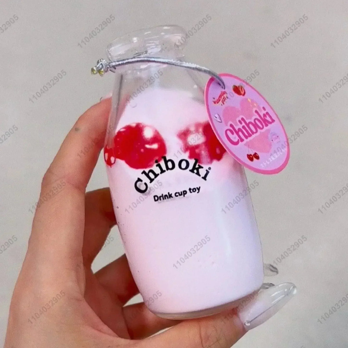 A hand holds a clear bottle filled with pink liquid and red fruit shapes, labeled as a Chiboki drink cup toy.