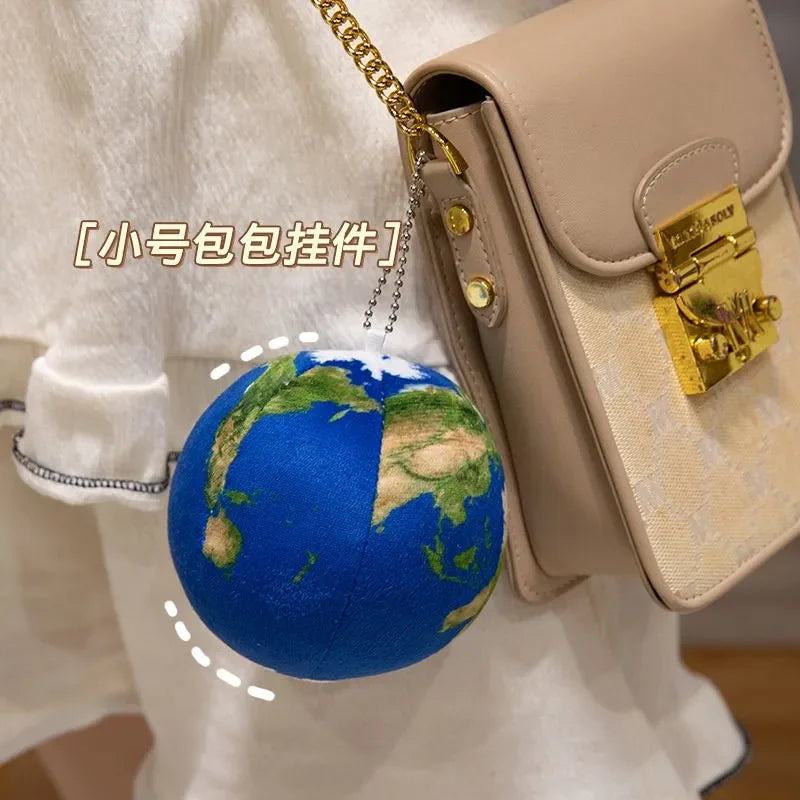 A beige leather pouch with a gold clasp and a blue globe plush toy attached by a chain.