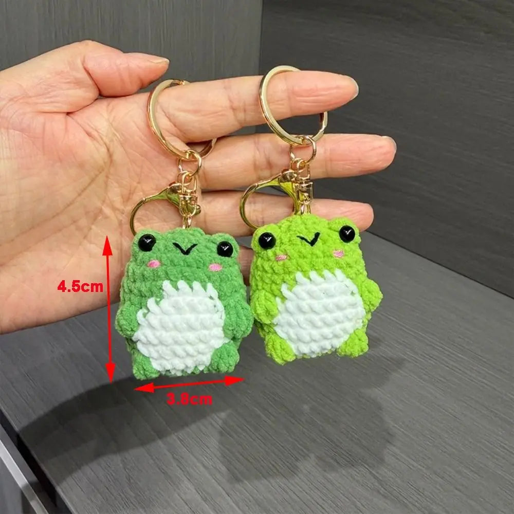 A pair of handmade crochet frog keychains with gold-colored rings and soft green and white yarn bodies.