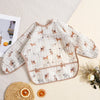 A beige and white patterned waterproof long sleeve feeding bib for babies lying on a light surface with citrus fruit.