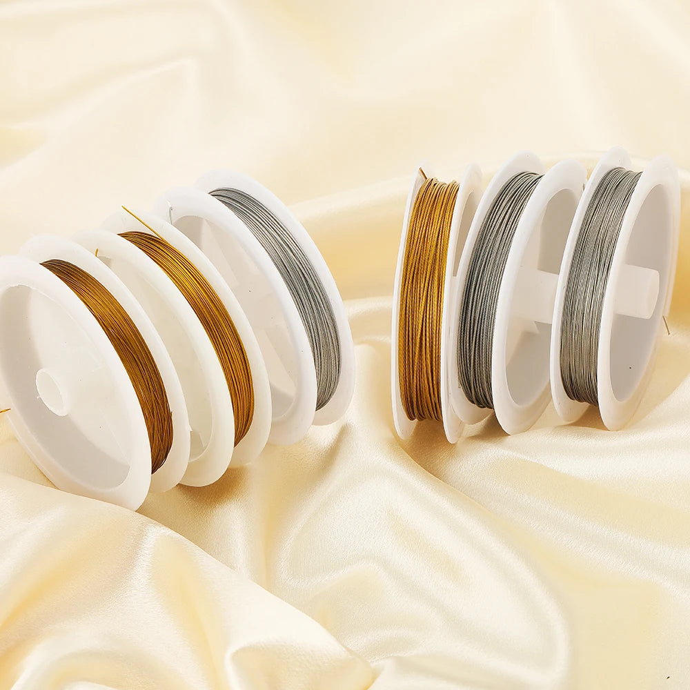 Rolls of stainless steel beading wire in gold and silver colors displayed on silk fabric.