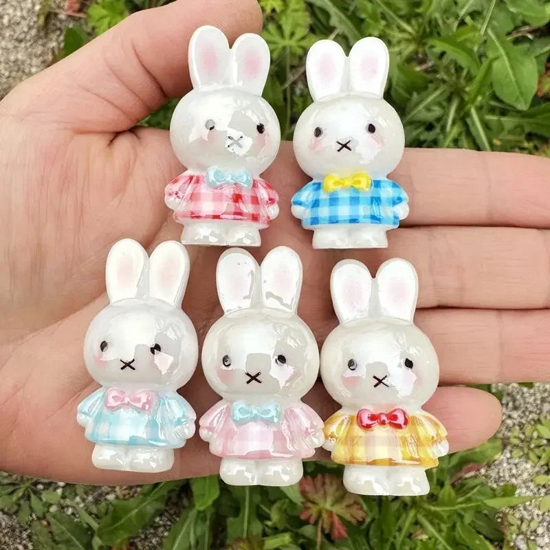 A hand holds several white resin bead charms shaped like rabbits in various colors and styles.