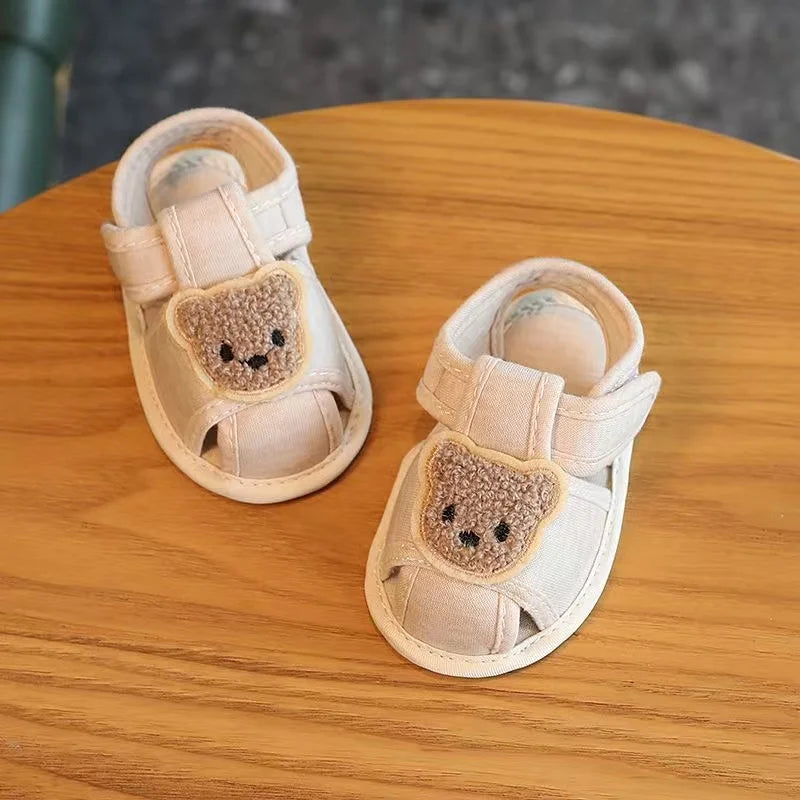 Pair of beige soft sole first walker shoes shaped like bears for babies resting on a wooden surface.