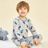 A smiling young boy wearing a light blue long-sleeved cotton pajama set with an astronaut print, sitting on a white surface.