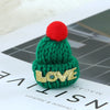A handmade green knitted Christmas hat with a red pompom and gold LOVE lettering on the front.