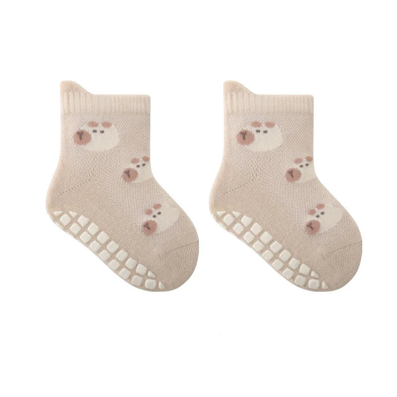 A pair of light beige knitted socks featuring a cute cartoon bear design and non-slip grips on the sole.