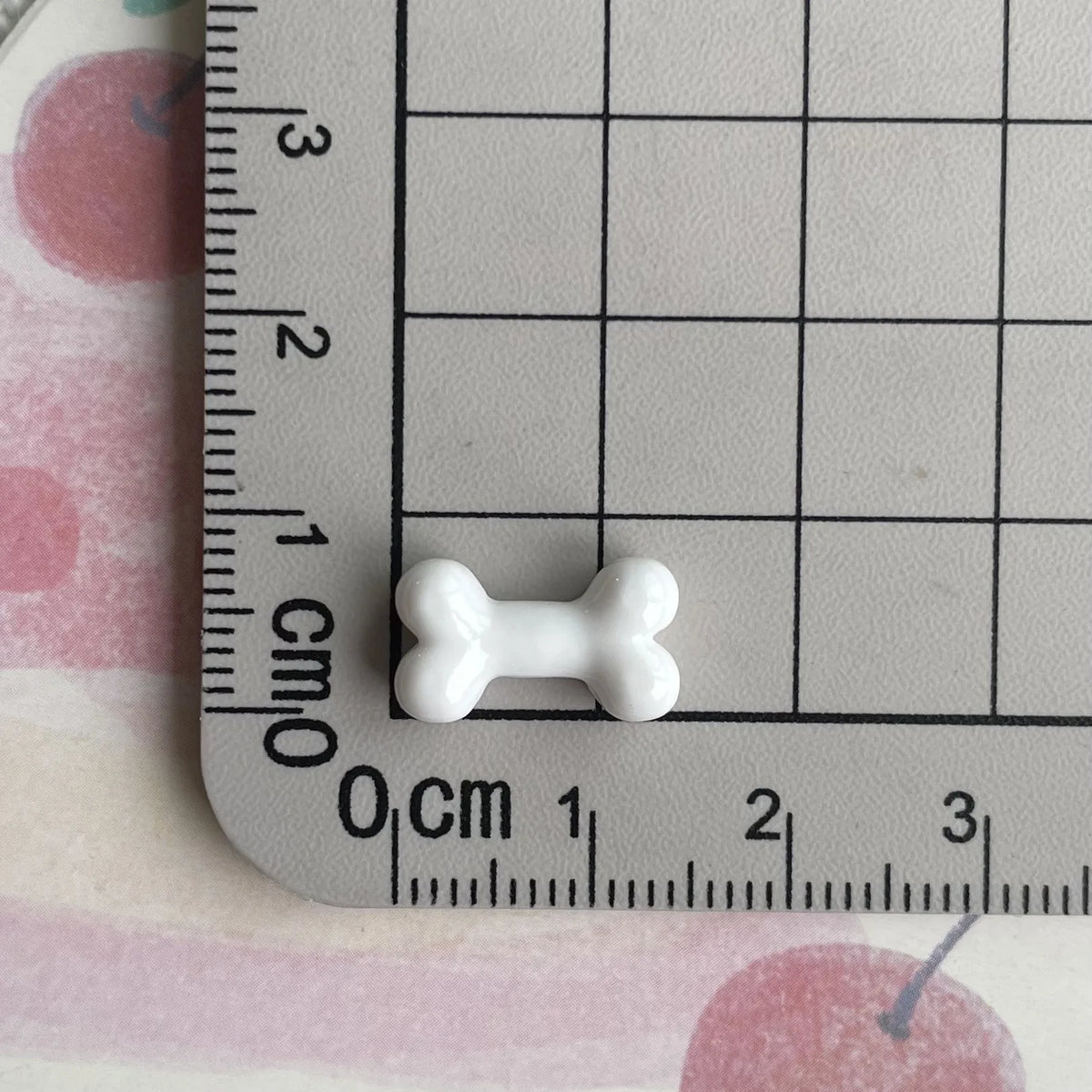 A small white resin bone charm is placed on a ruler marked in centimeters and inches.