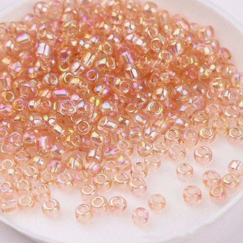 A pile of small, translucent pink and orange glass rice beads for DIY jewelry and crafting.