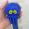 A hand holds a bright blue squeeze and soak octopus bath toy for toddlers with yellow eyes.