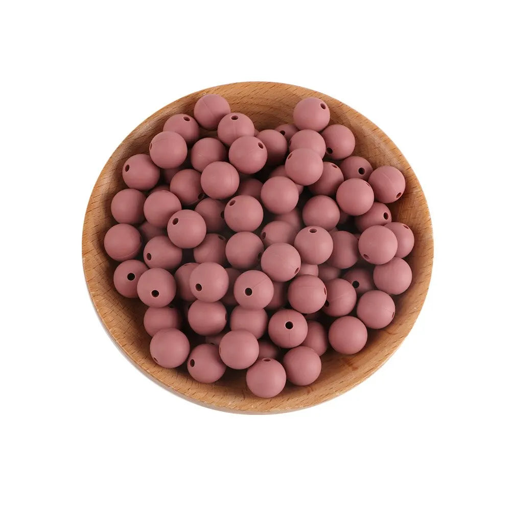 A wooden bowl filled with small, round, pink silicone beads for jewelry making and crafts.